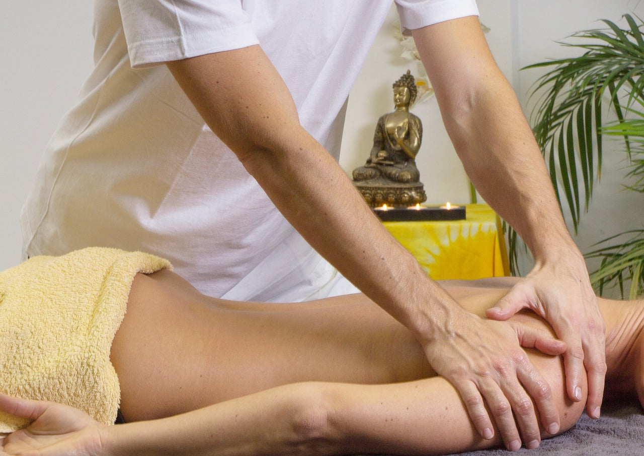 Person receiving a massage with a focus on the hands and arms, in a setting with a Buddha statue and plant.