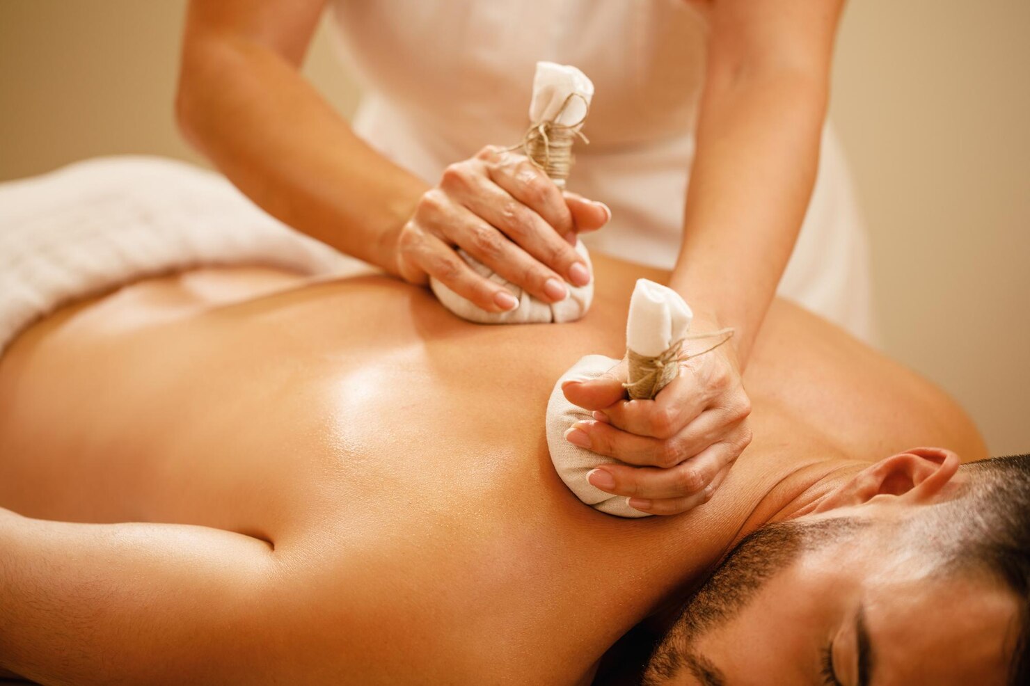 Person receiving a massage with white towels and a bottle of oil.